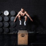 Young strong fit sweaty muscular man with big muscles doing box jump workout in the gym as hardcore cross training